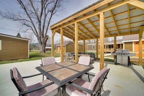 Un patio techado al aire libre con mesa y sillas, una parrilla y vistas a casas vecinas.