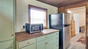 Una cocina con microondas, refrigerador, encimera de madera y armarios verde claro.
