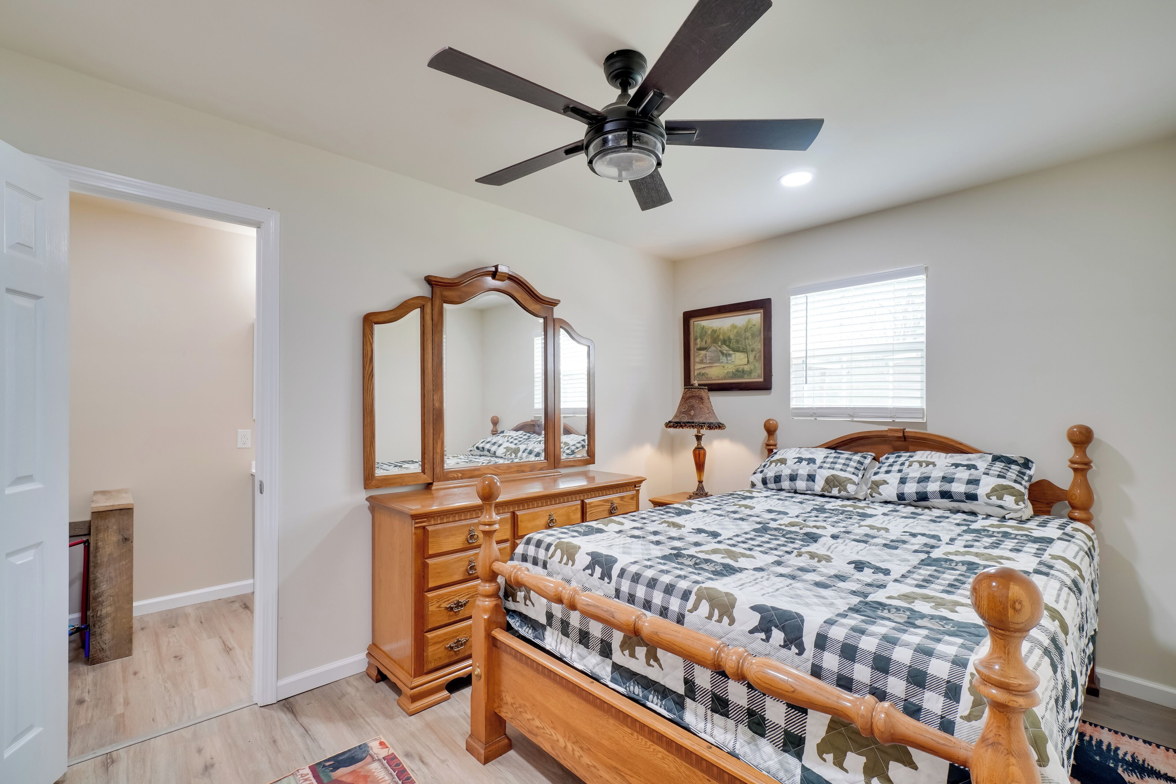 A bedroom with a bed, a dresser, a ceiling fan, a mirror, a window, and a door.