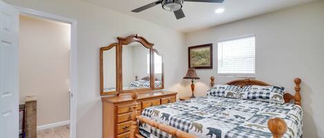 A bedroom with a bed, a dresser, a ceiling fan, a mirror, a window, and a door.