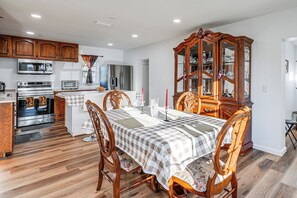 Un coin repas avec une nappe à carreaux, des chaises en bois, un buffet en bois et une cuisine en arrière-plan.