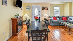 Et spiseområde med et træbord, stole og en pejs. Der er en opholdsstue med en sofa og et fjernsyn.