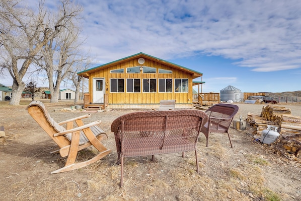 A rustic wooden cabin with large windows, a porch, and a fenced yard with wooden rocking chairs.