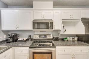Una cocina con gabinetes blancos, microondas de acero inoxidable, cafetera y tostadora.
