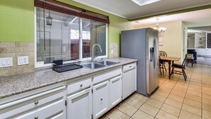 Una cocina con encimera de granito, armarios blancos, pileta de acero inoxidable y refrigerador gris.