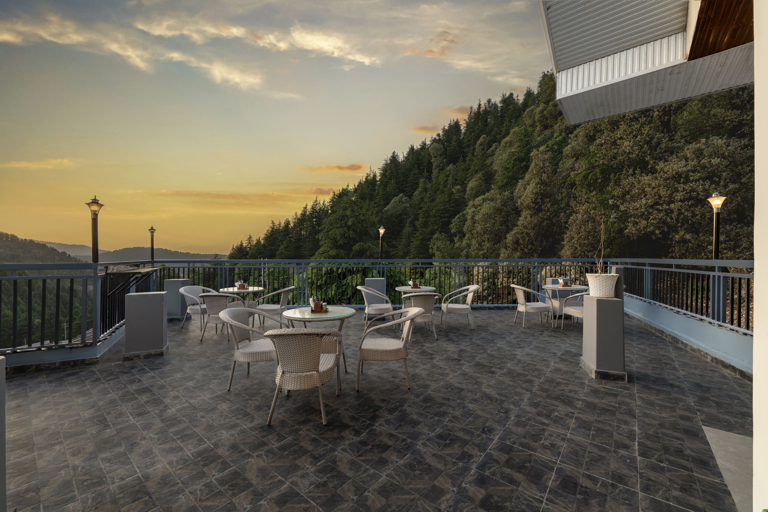 A terrace with outdoor seating, a view of a forested hillside, and a building with a modern design.