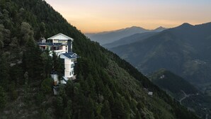 A mountain lodge with a balcony, surrounded by dense forest and distant mountains. - Echor Alpine Meadows Khajjiar Dalhousie (Chamba)