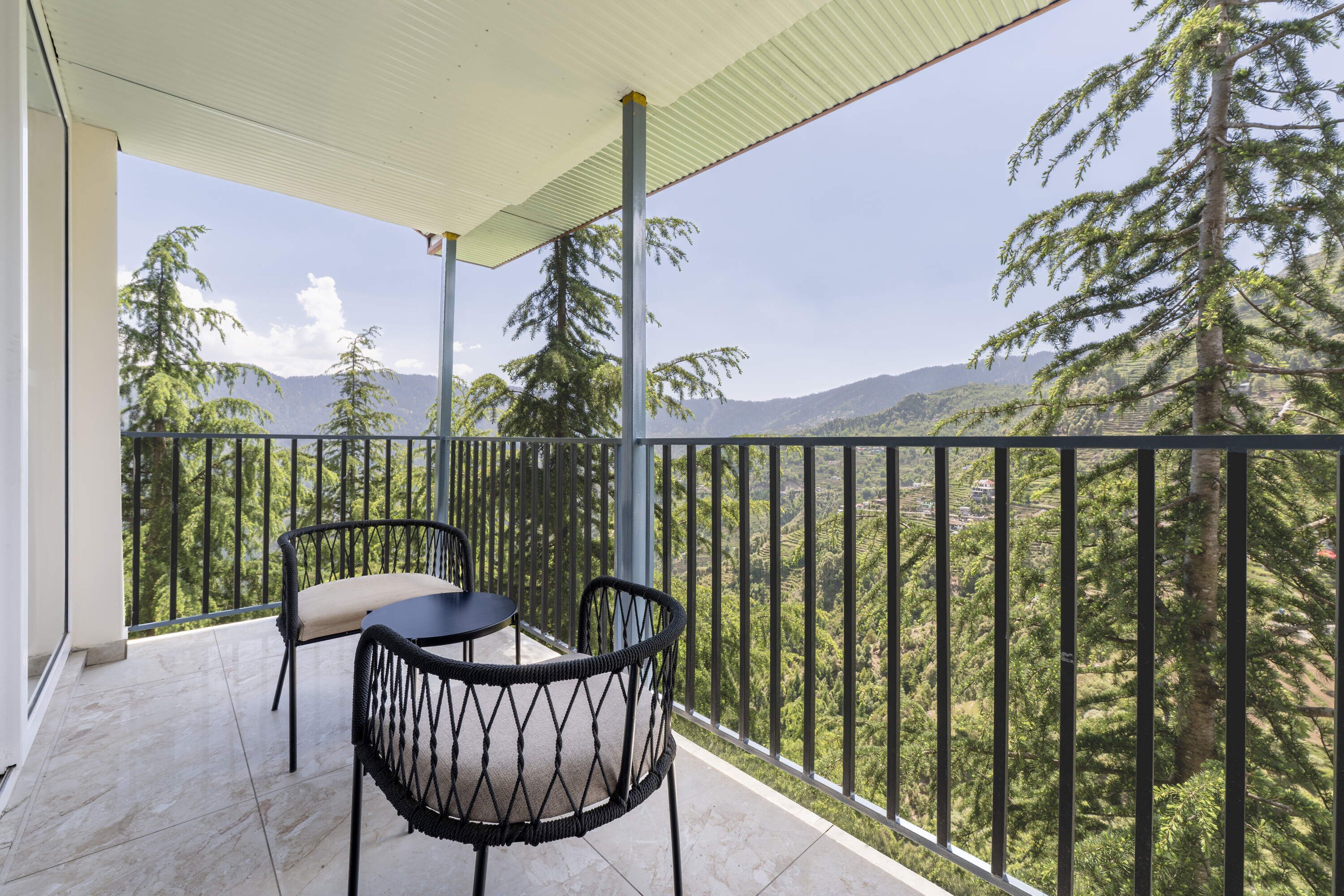 Un balcón con dos sillas y una mesa, con vistas a un paisaje montañoso de árboles densos.