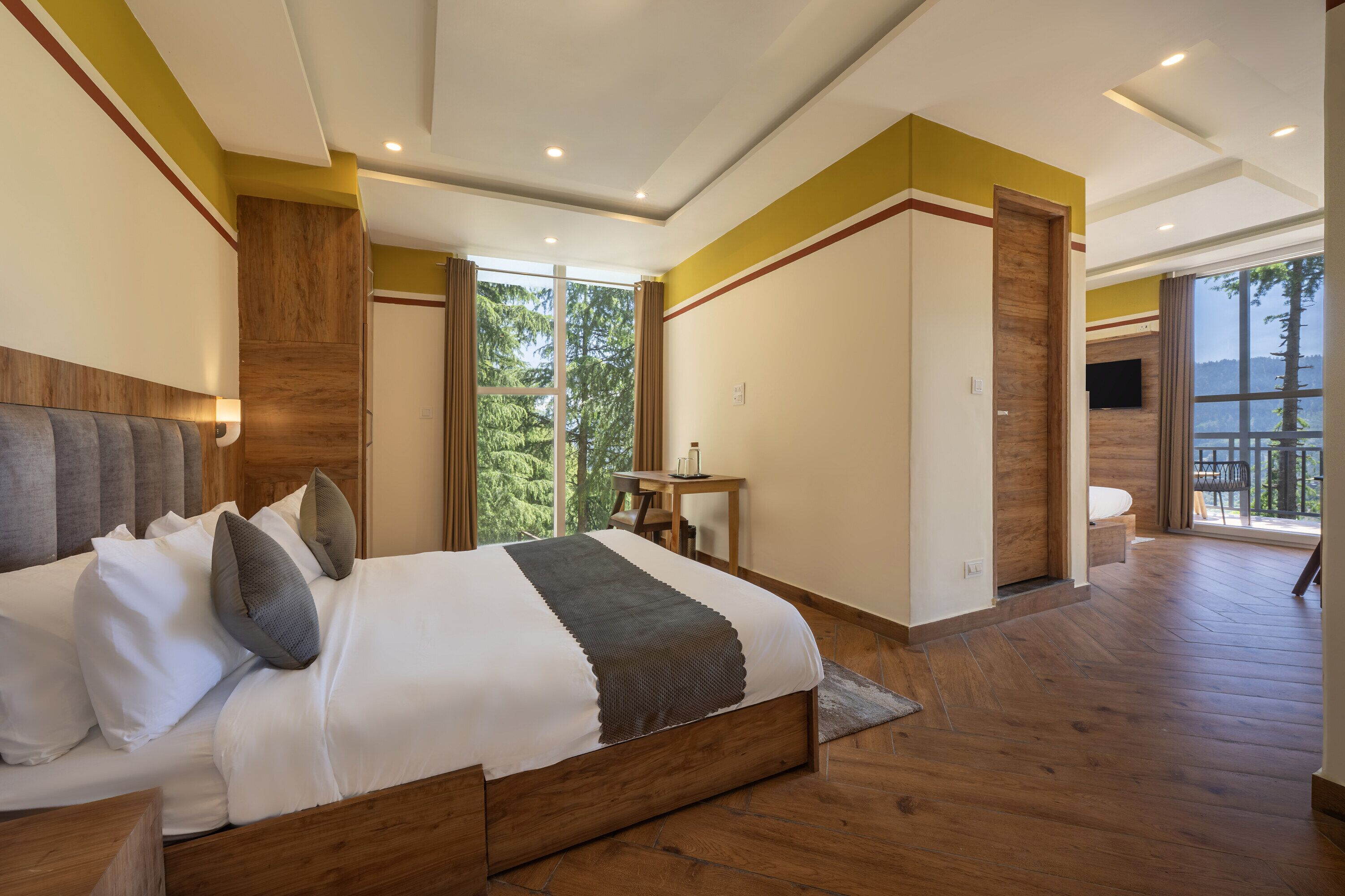 Une chambre moderne avec un grand lit, un plancher en bois, une télévision et une vue sur l’extérieur.