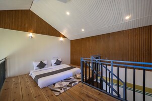 A bedroom with a wooden floor, a bed with white bedding, a blue railing, and a sloped ceiling with recessed lighting.