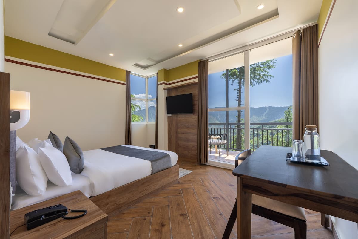 Habitación de hotel con cama, escritorio, televisor y balcón con vista a la montaña.