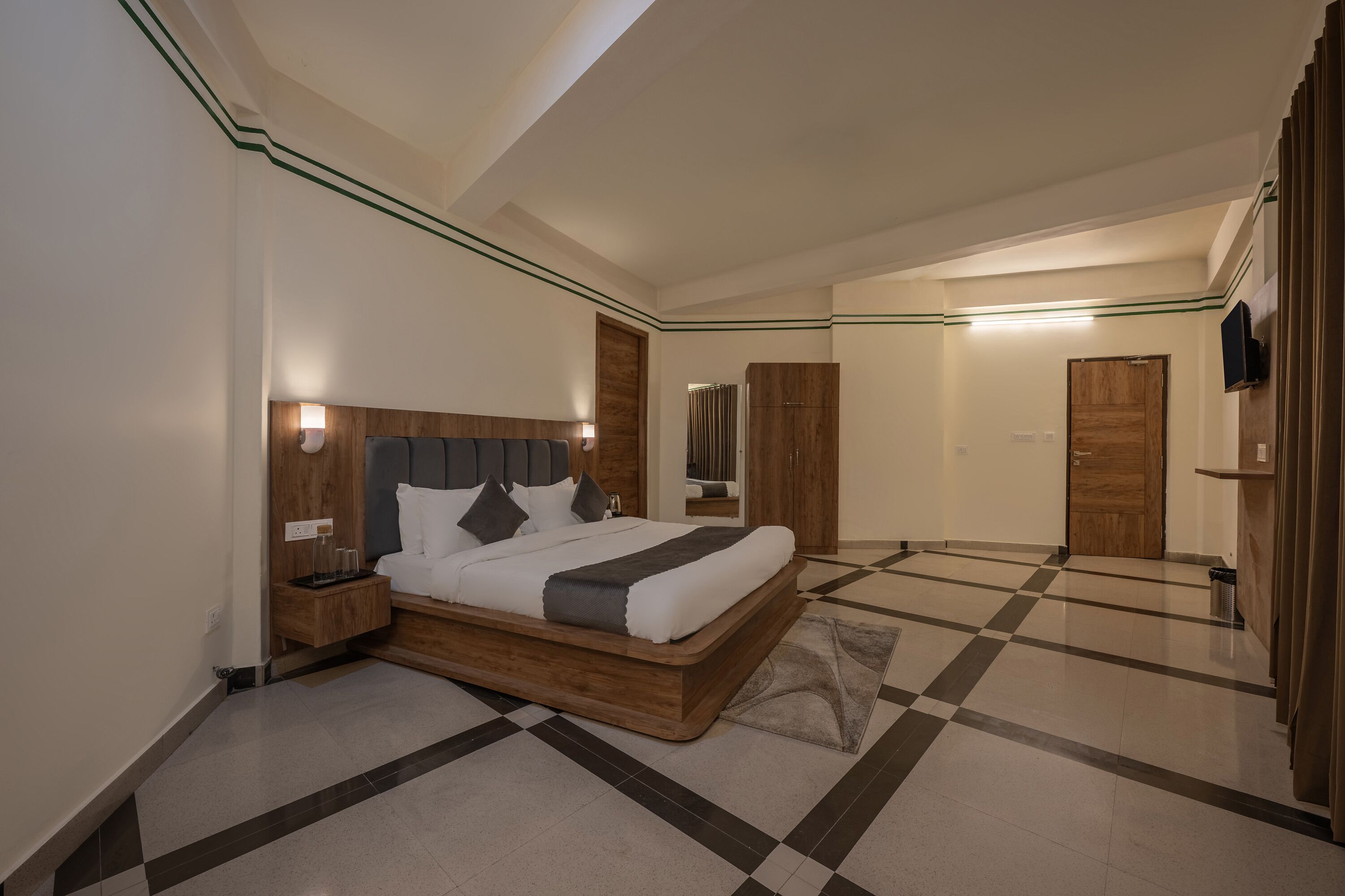 Une chambre d’hôtel moderne avec un grand lit, une tête de lit en bois et un motif de carreaux au sol.