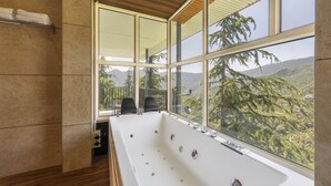 A modern bathroom with a large bathtub, wooden ceiling, and a view of mountains through large windows. - Echor Alpine Meadows Khajjiar Dalhousie (Chamba)