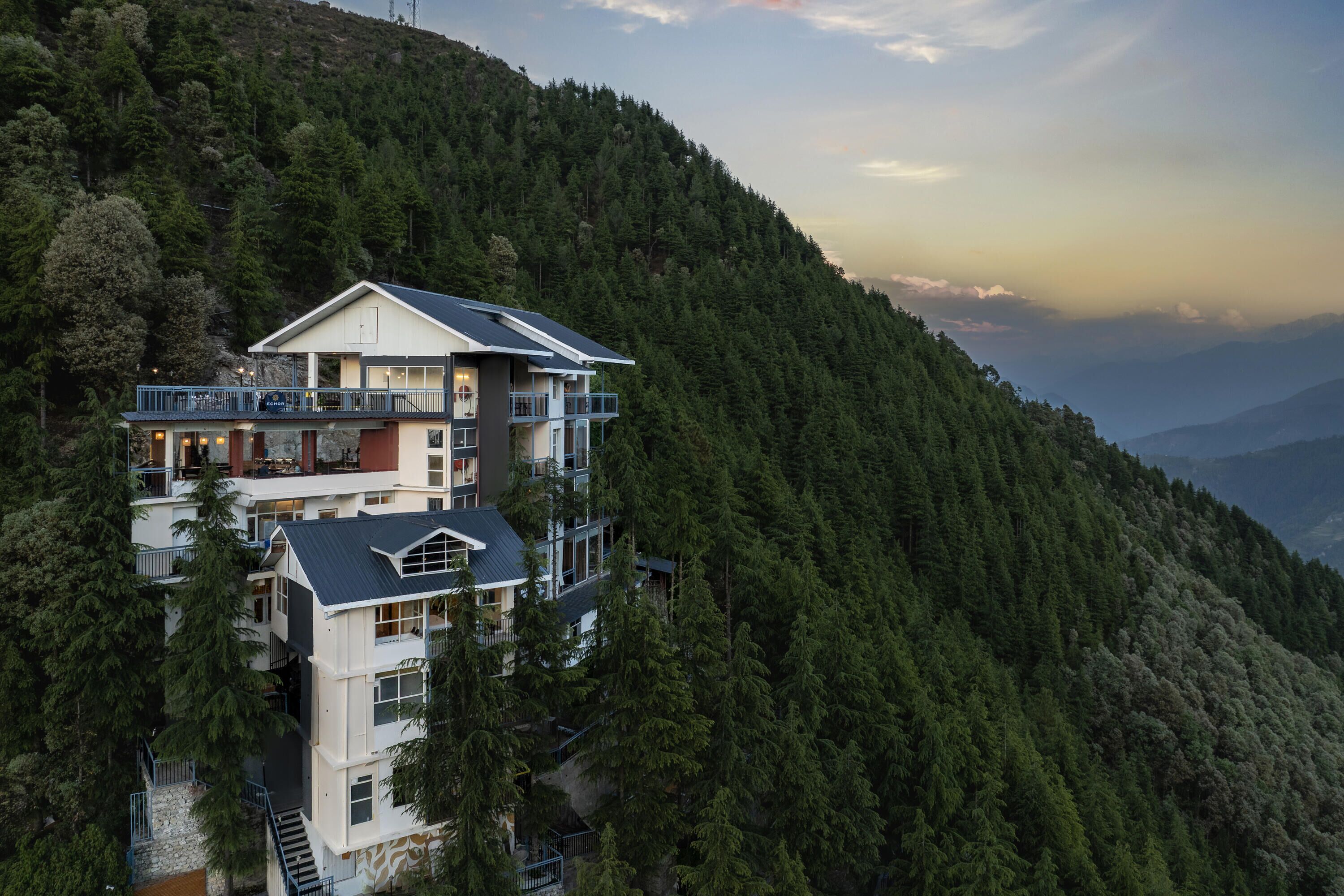 A multi-story building with balconies, surrounded by dense forest.