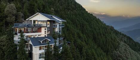 A multi-story building with balconies, surrounded by dense forest.