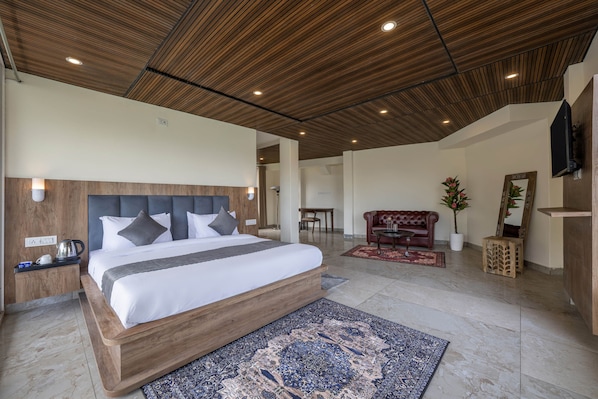 A modern bedroom with a wooden headboard, a large bed, a nightstand, a coffee maker, a TV, a red sofa, a potted plant, and a mirror. - Echor Alpine Meadows Khajjiar Dalhousie (Chamba)