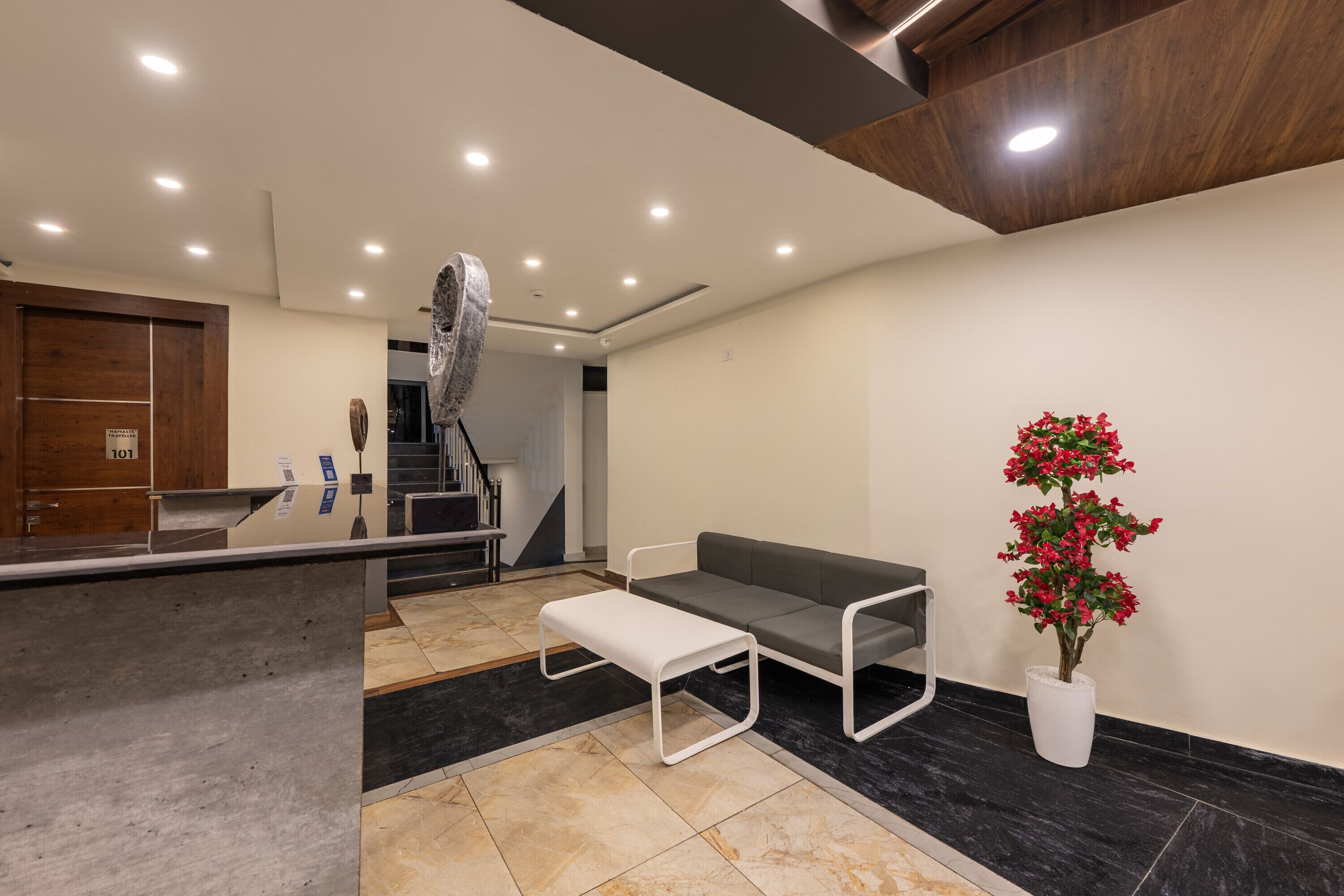 A modern reception area with a reception desk, a grey sofa, a white bench, and a potted plant.