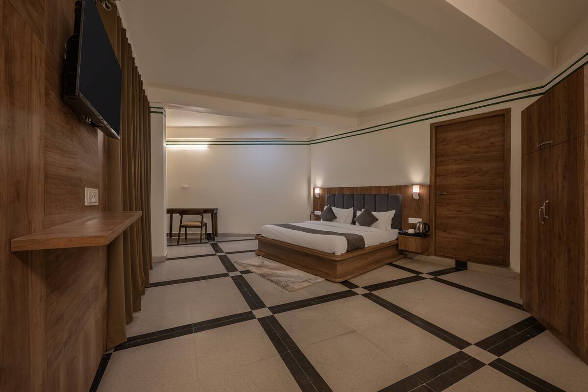 Una habitación de hotel con piso a cuadros, una cama con cabecera de madera, un televisor montado en la pared y un armario.