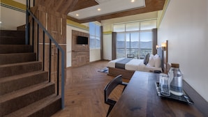 A modern hotel room with a wooden staircase, a sofa bed, a dining table, and a view of mountains. - Echor Alpine Meadows Khajjiar Dalhousie (Chamba)