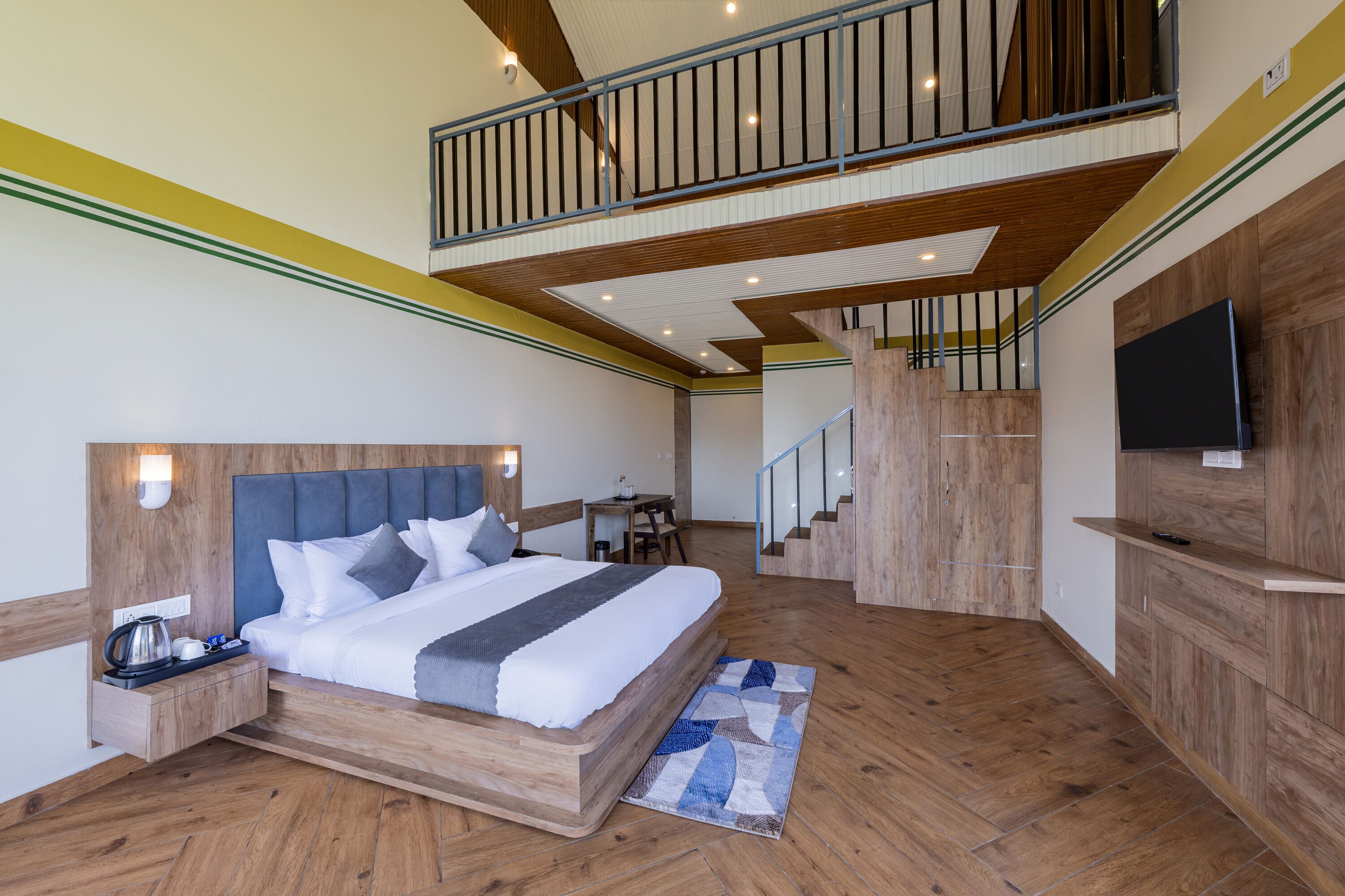 A modern hotel room with a large bed, wooden flooring, a balcony, and a TV on the wall.