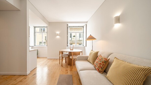 Una sala de estar moderna con un sofá, una mesa de comedor con sillas, una lámpara y vistas al exterior.