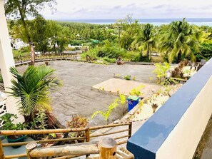 A view from a balcony overlooking a courtyard with a pool, surrounded by tropical vegetation and a distant ocean view. - Casa Lakot (Rodrigues Island)