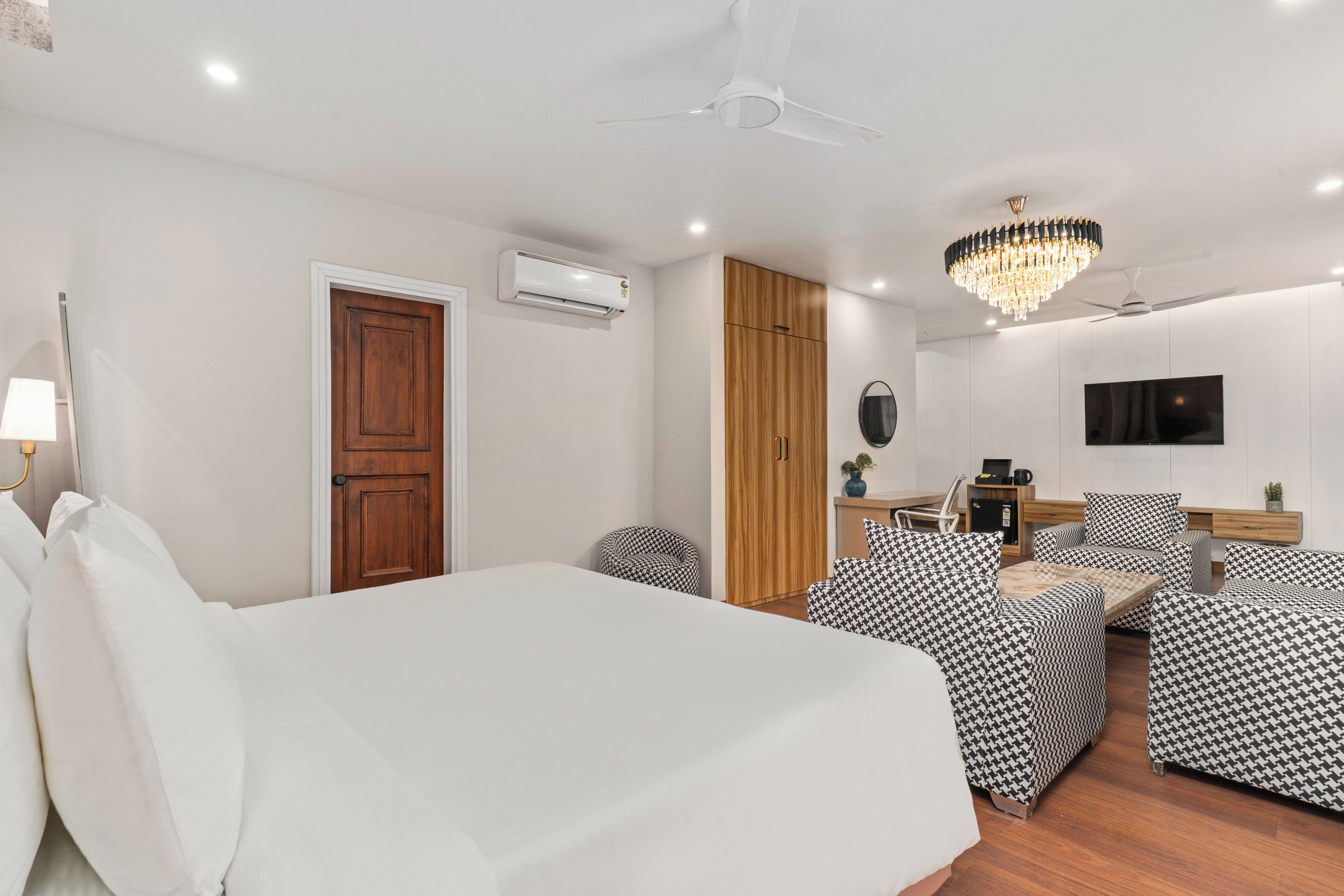 Ein modernes Hotelzimmer mit Bett, Sofa, Sesseln, Fernseher und Deckenventilator.