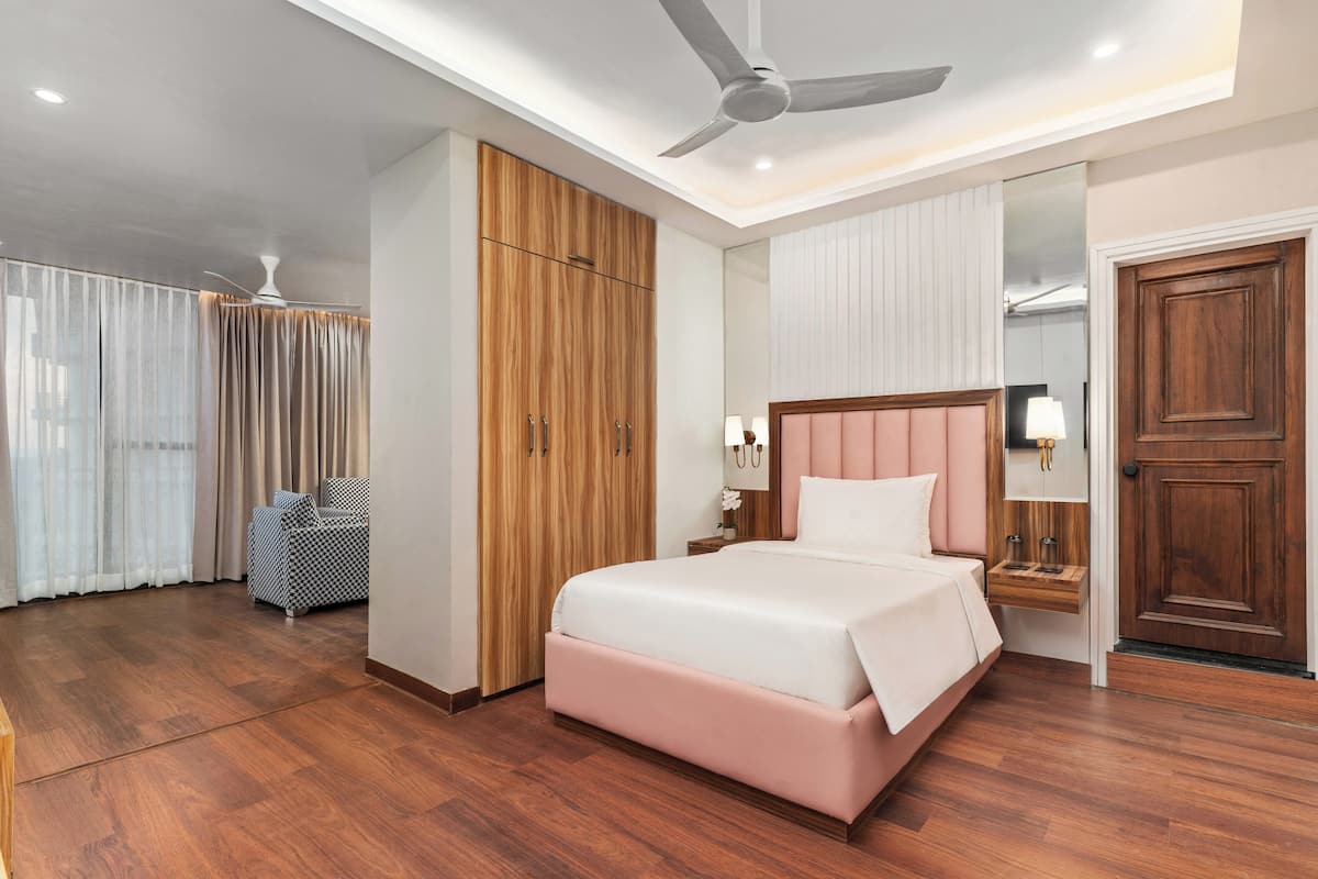 Una camera d'albergo con un letto, un armadio, un comodino, una lampada e una ventola a soffitto.