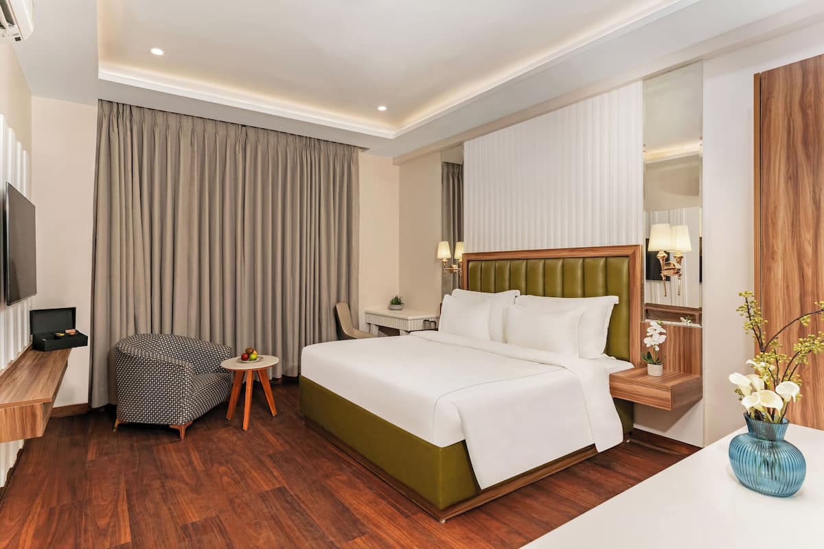 Camera d'albergo con un letto grande, una scrivania, una sedia, una televisione e un vaso con fiori.