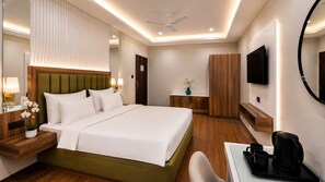 A hotel room with a bed, bedside table, lamp, mirror, TV, wardrobe, and a desk with a coffee maker. - Country Inn Rishikesh (Rishikesh)