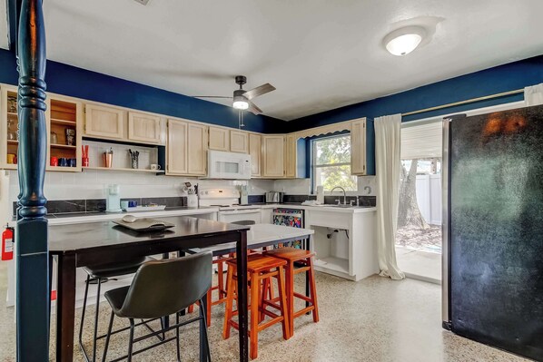 Una cocina con una isla central, taburetes de madera, microondas y ventilador de techo.
