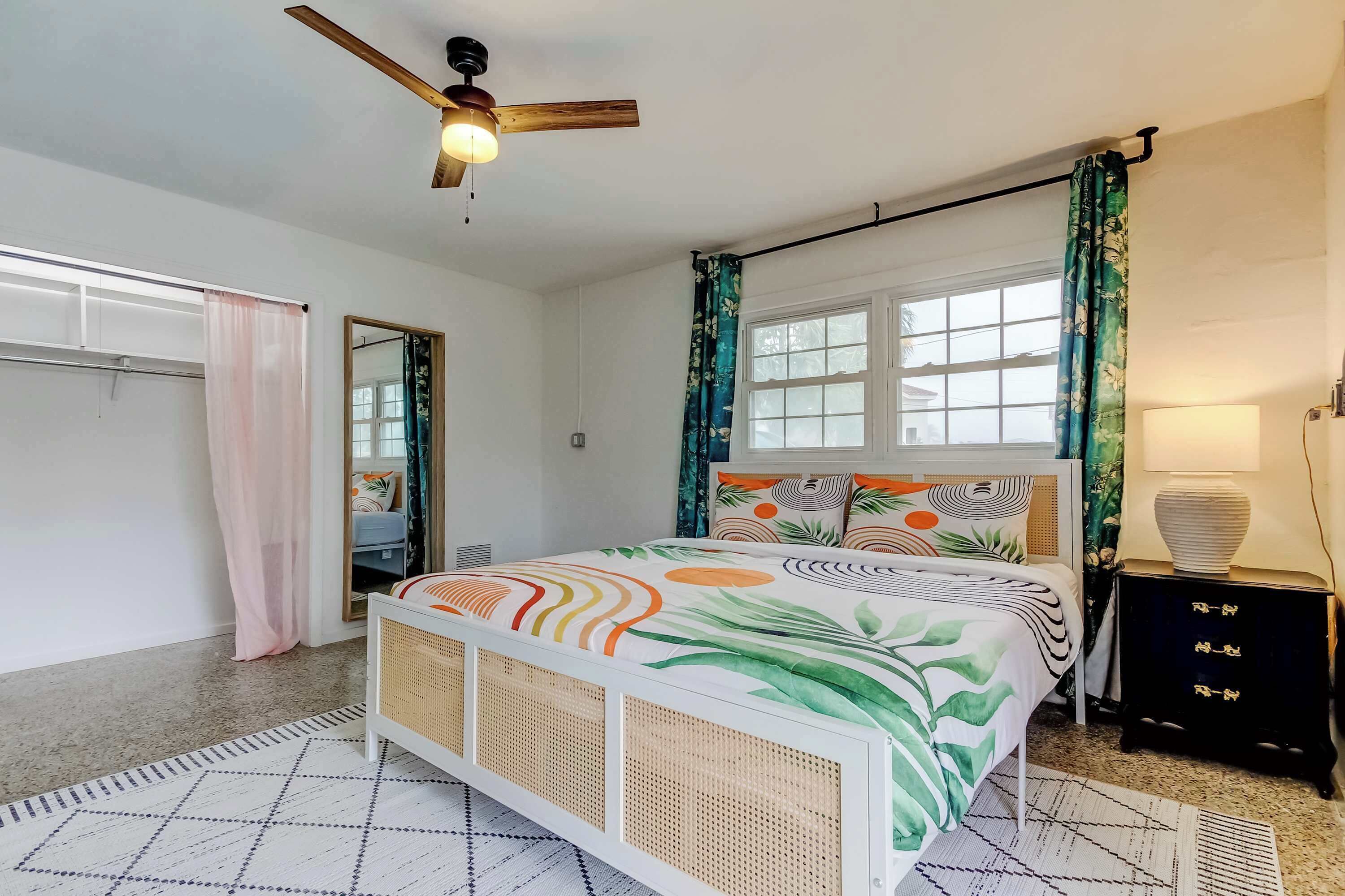 A bedroom with a bed, a ceiling fan, a window with curtains, a bedside table, and a nightstand.