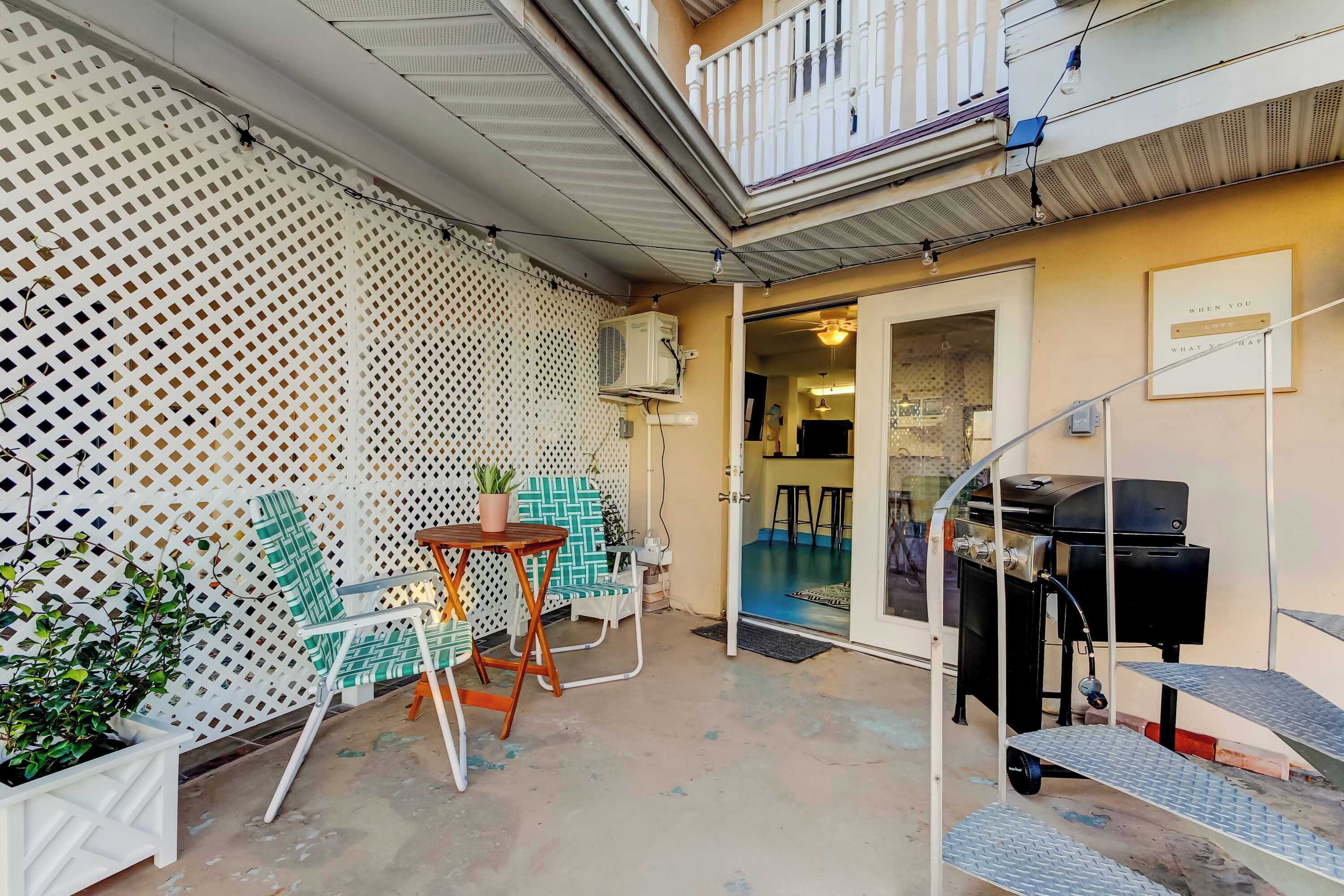 A balcony with a white lattice partition, a table with chairs, a grill, and a small staircase.