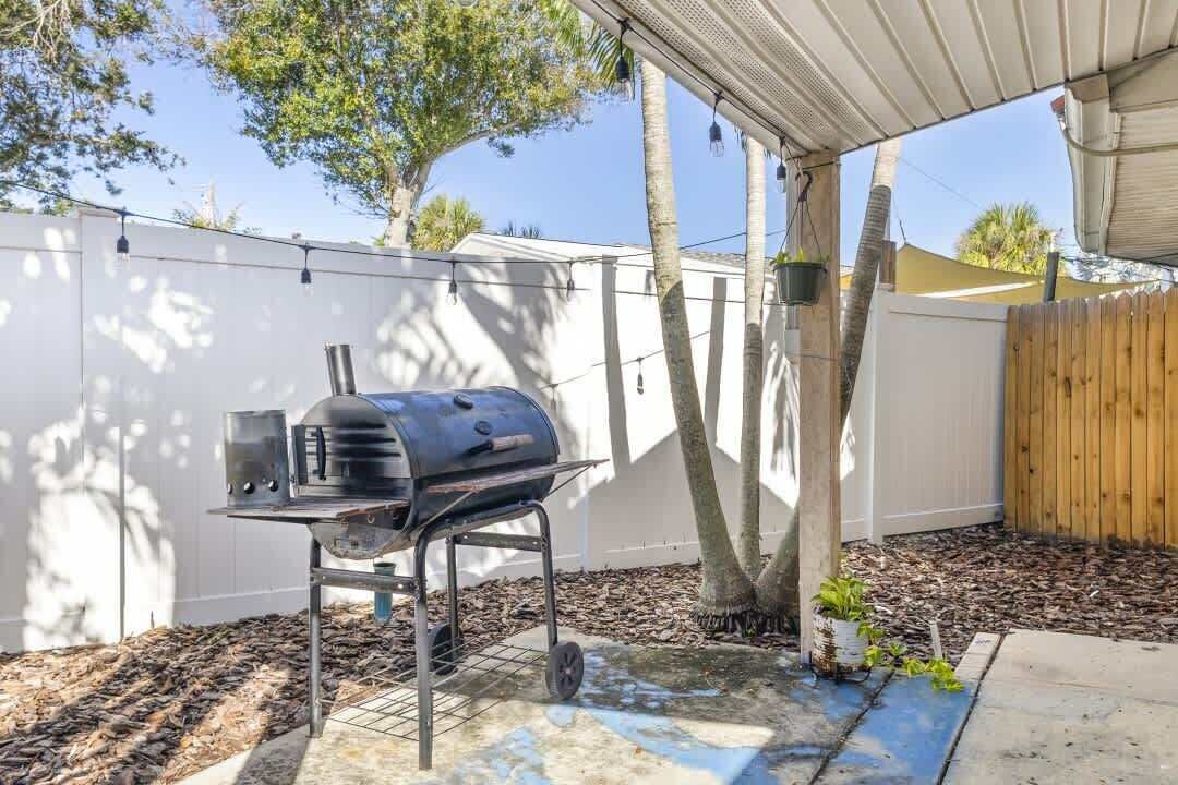 A backyard with a portable grill, a wooden fence, and a tree.