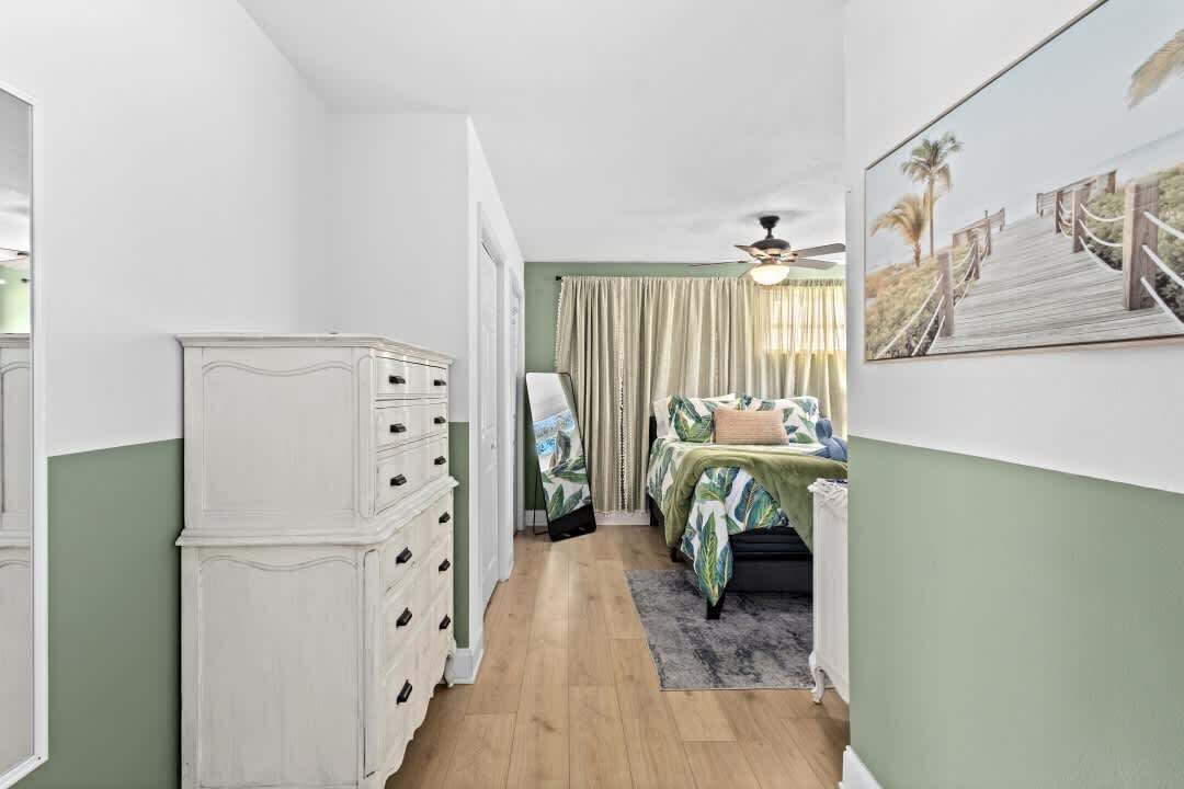 A bedroom with a bed, a dresser, a ceiling fan, and a painting on the wall.