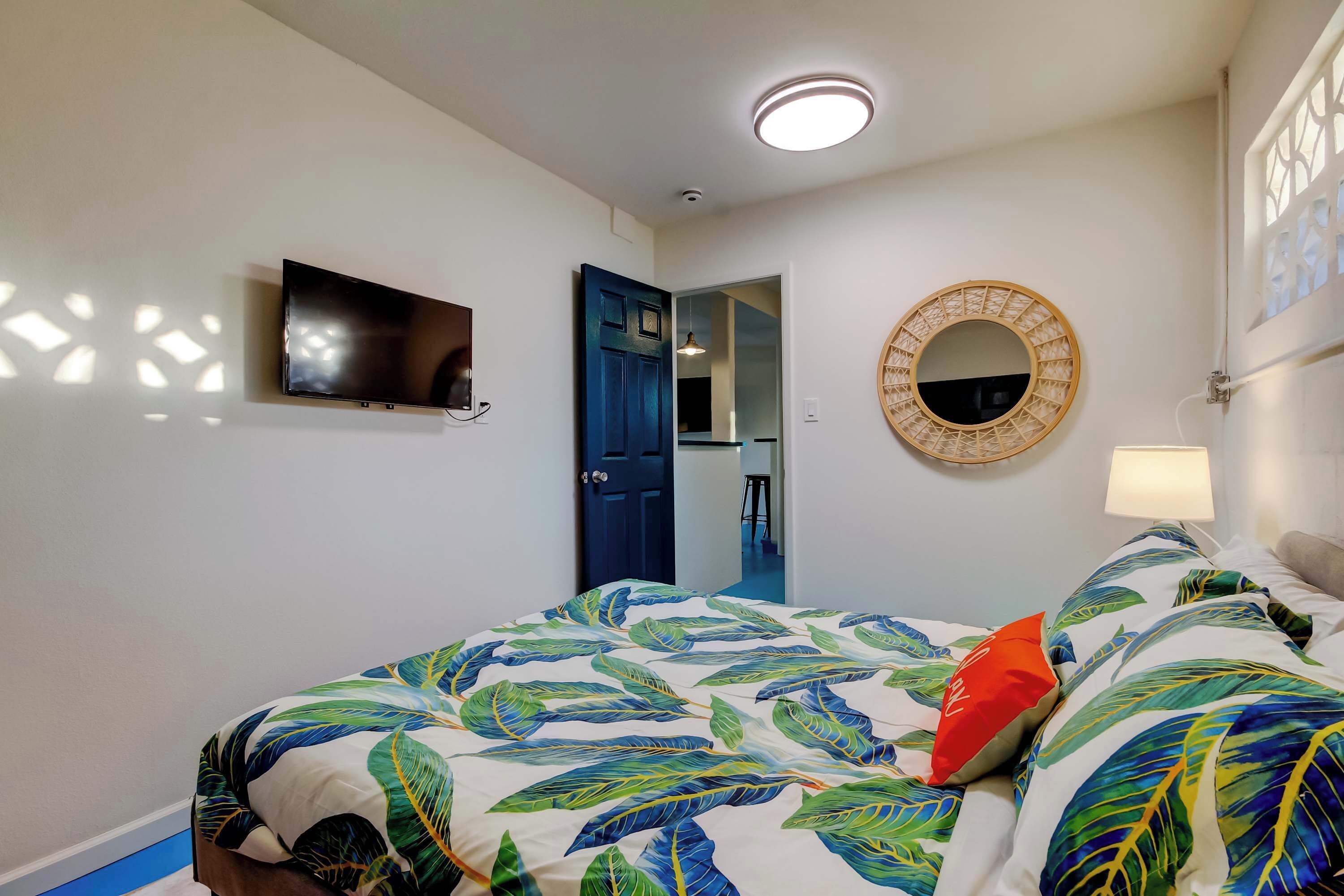 A bedroom with a bed, a TV, a mirror, and a door leading to another room.