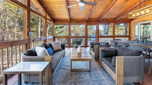 Ein überdachter Außenbereich mit Holzbalken, einem Deckenventilator und Möbeln, darunter Sofas und ein Tisch.