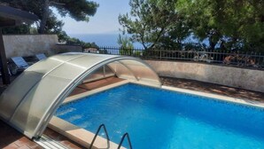 A swimming pool with a glass enclosure, surrounded by a stone wall and trees. - Studio with shared pool (Stanići)
