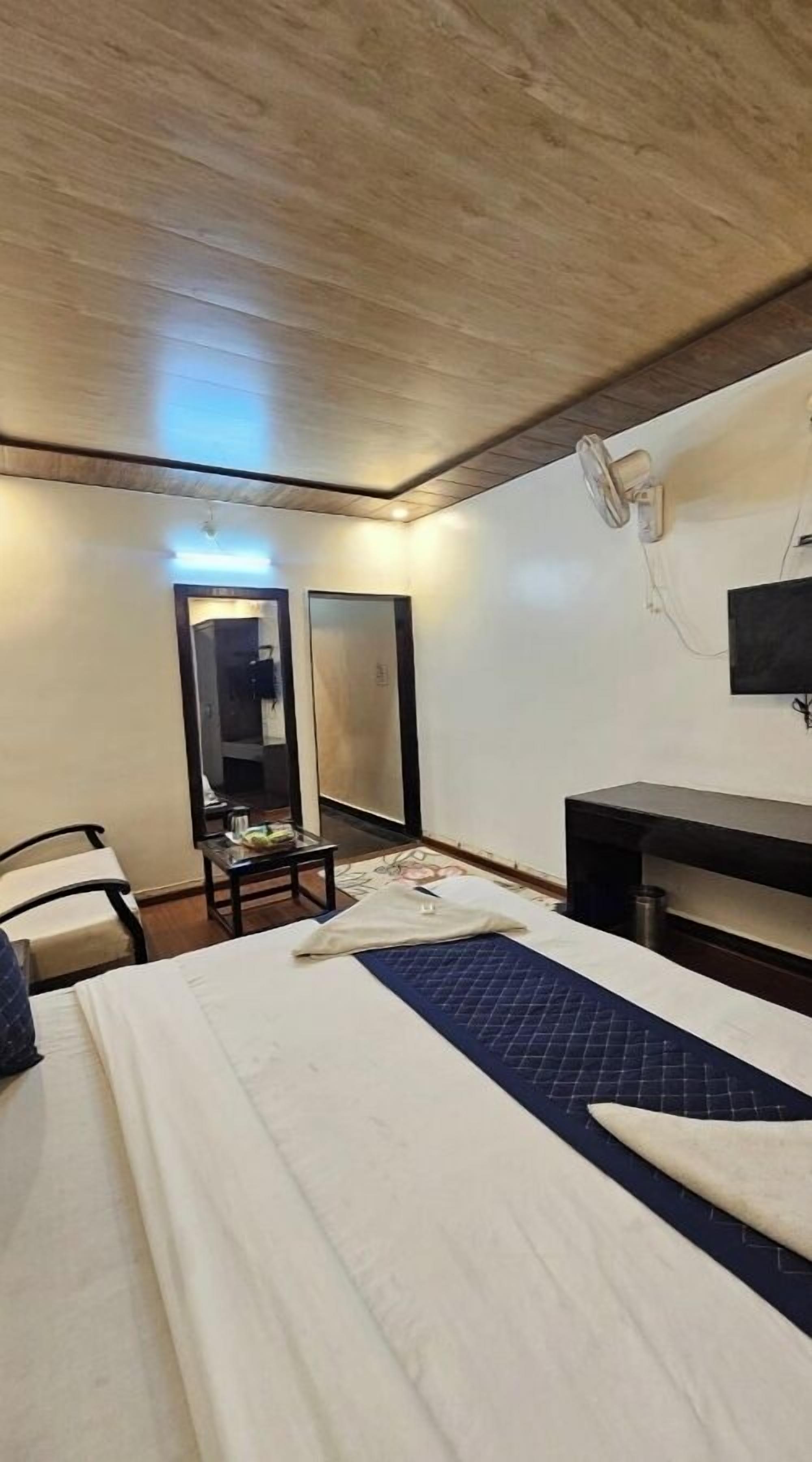 A hotel room with a bed, a desk, a chair, a mirror, and a television.
