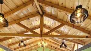 Ein geräumiger Essbereich mit Holztischen und -stühlen, großen Fenstern und einer hohen Holzdielendecke mit hängenden Lampen.