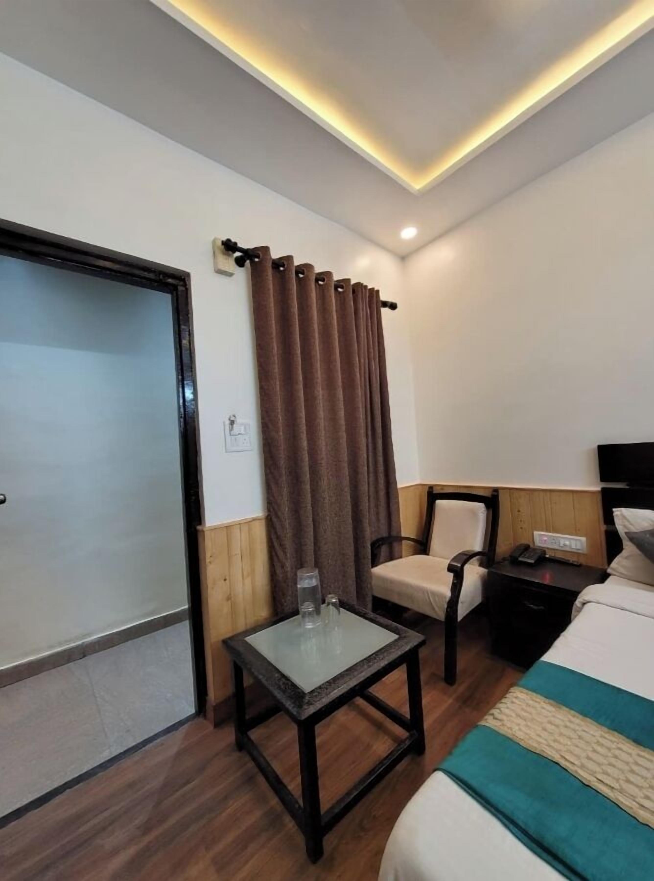 A hotel room with a bed, a small table with a glass, a chair, a nightstand, and a curtain.