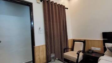 A hotel room with a bed, a small table with a glass, a chair, a nightstand, and a curtain.