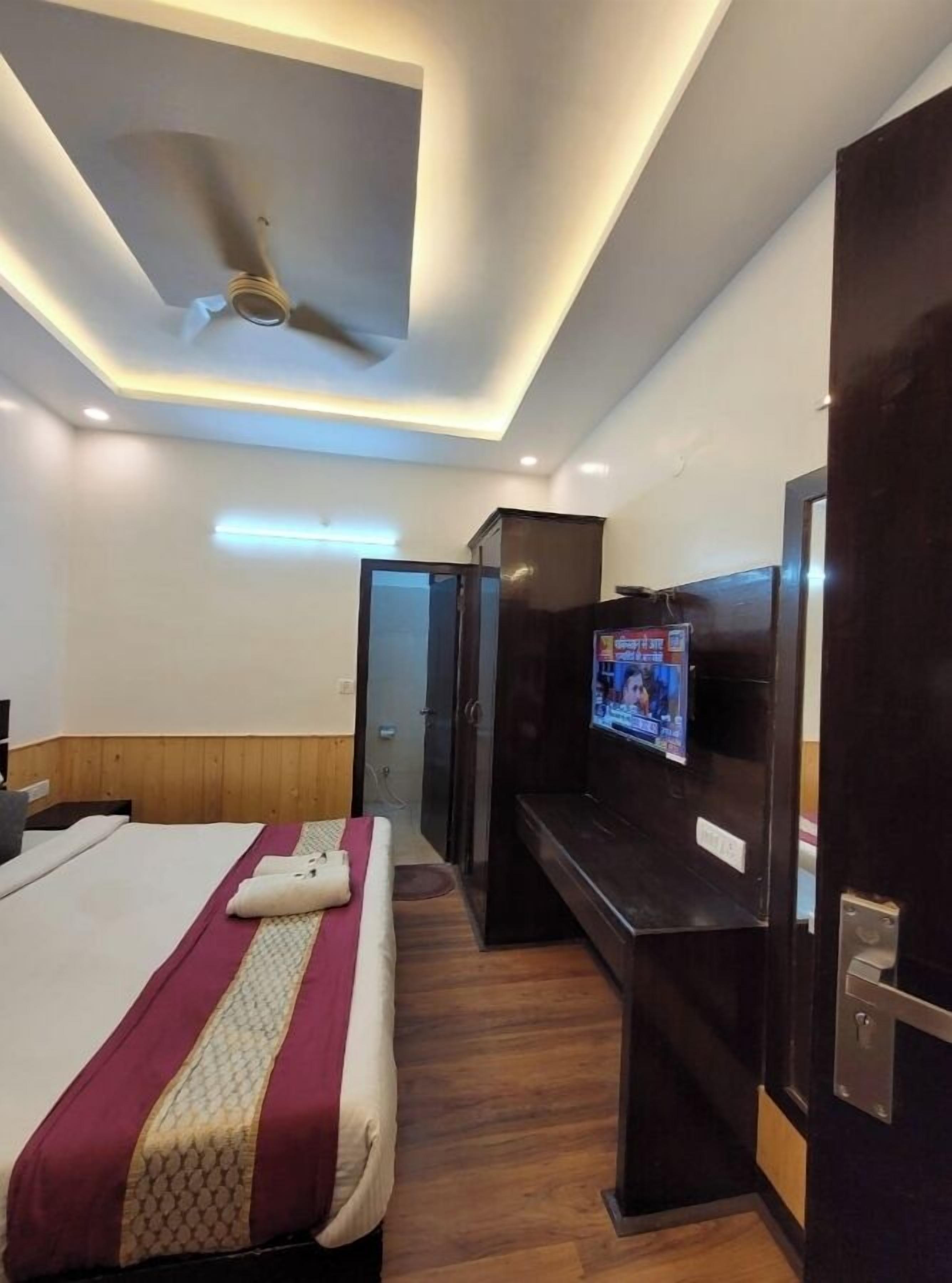 Una habitación de hotel con cama, televisor, ventilador de techo y piso de madera.