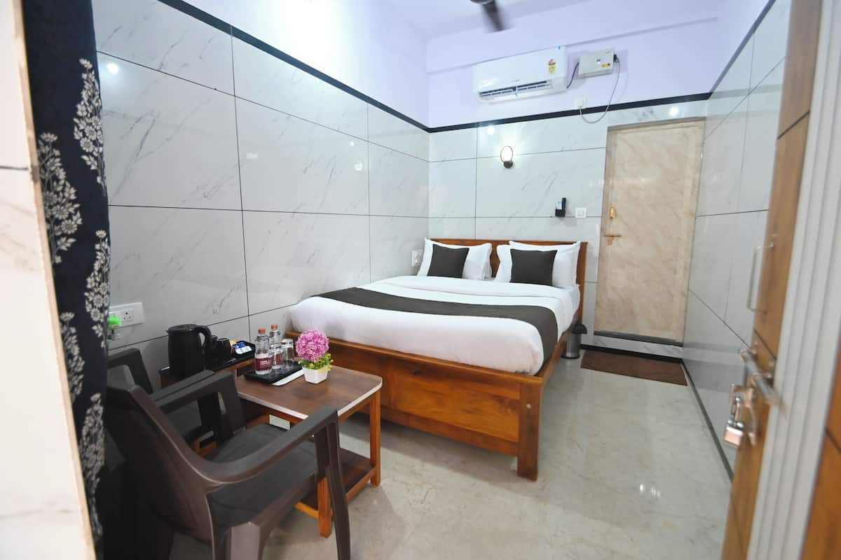 Quarto de hotel com cama, escrivaninha com cadeira, mesa pequena com flor e guarda-roupa.