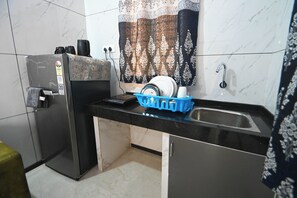Een kleine keuken met een koelkast, een wastafel en een blauwe afwasslede.