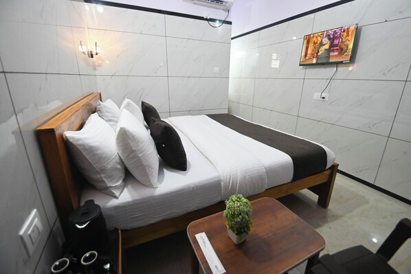 A hotel room with a bed, bedside table, and a small potted plant. - CR7 Stay Rooms and Homestay (Murudeshwara)