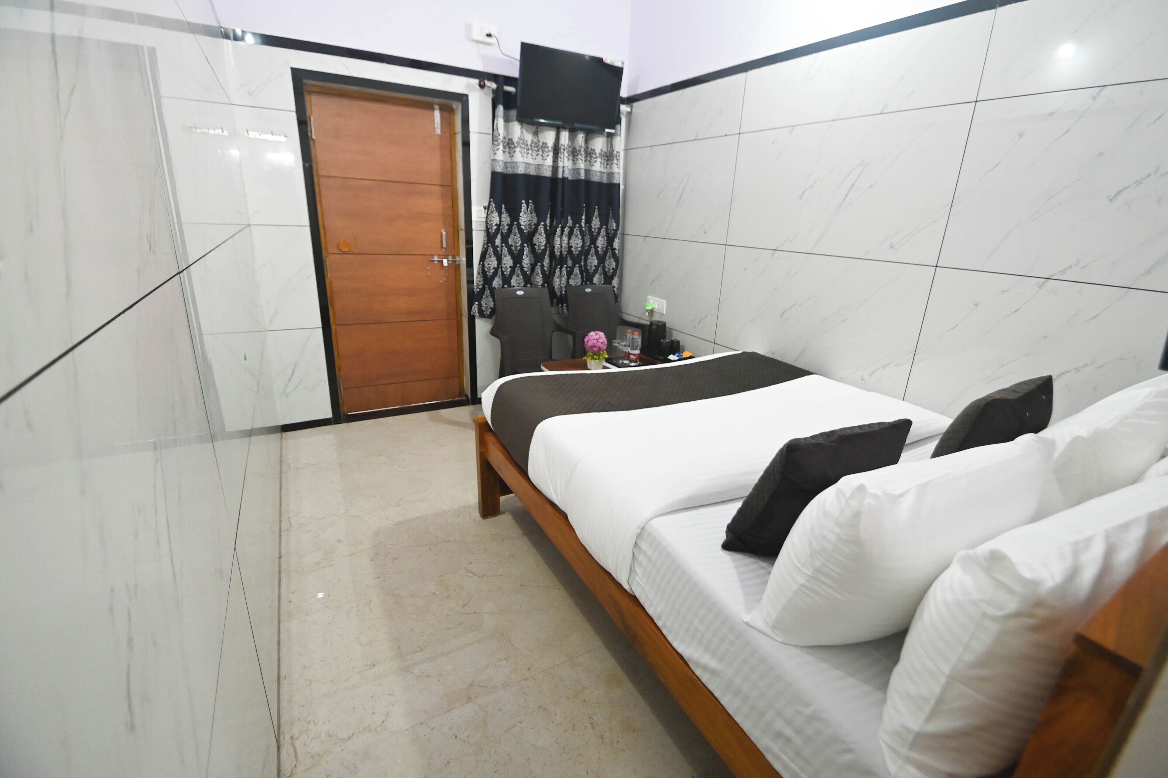 A bedroom with a bed, a wooden door, a TV mounted on the wall, and a chair.