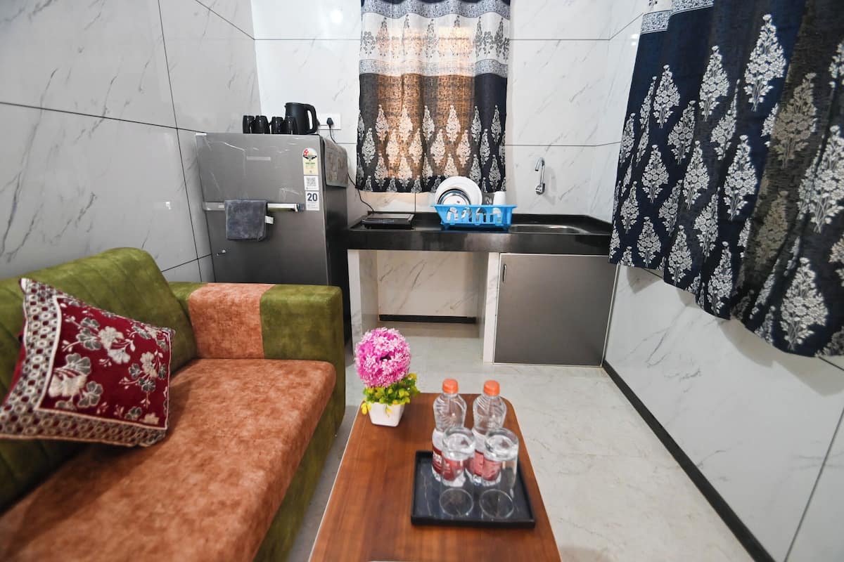 Um espaço compacto com sofá, uma mesinha com um vaso de flores e garrafas, frigorífico e micro-ondas.