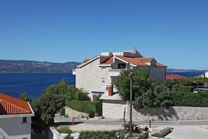 A coastal building with a stone facade, a red-tiled roof, and a view of the sea. - Holiday apartment with shared pool (Stanići)