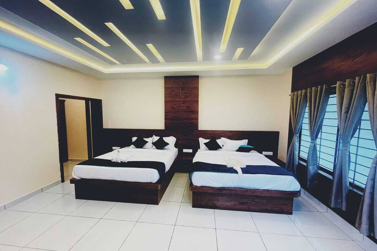 A hotel room with two beds, a wooden headboard, a ceiling with linear lighting, and a window with curtains.